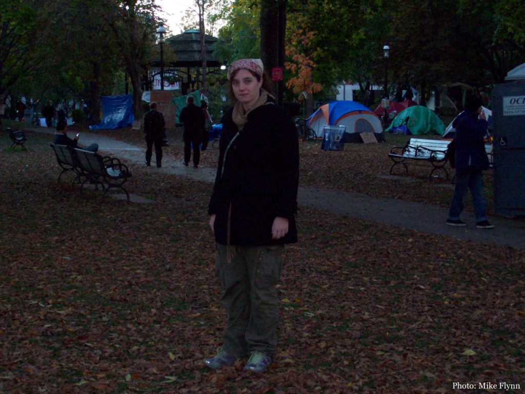 Megan Kinch, the article's author, stands in St. James Park in 2011, the tents of Occupy Toronto behind her.