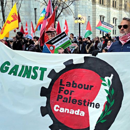 A protest march. A silver-haired man in a red keffiyah and sunglasses helps hold up a banner that reads "Labour Against Apartheid" and "Labour for Palestine Canada." Other protesters and Palestinian flags can be seen.