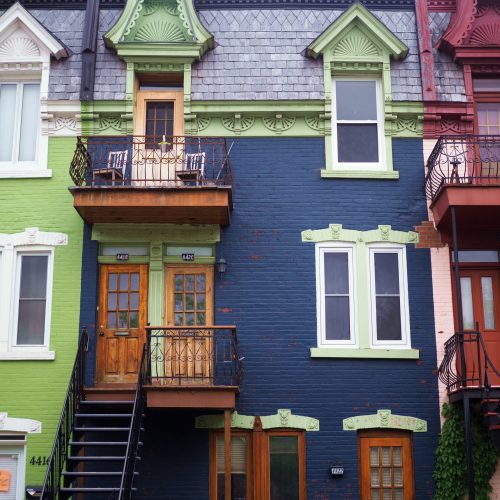 A strip of multicoloured townhouses in Montreal, with their distinctive long staircases. The houses are deep blue, light green, light pink; they have exquisite mouldings.